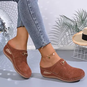 Detail of brown platform wedge mules with perforated floral patterns and metal buckle.