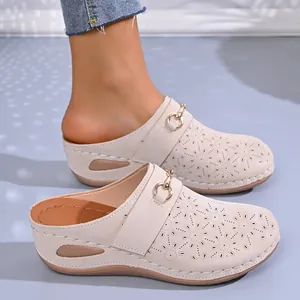 Detailed view of beige wedge mules with floral perforations and metal buckle on foot
