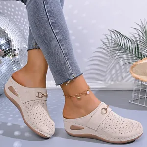 Detail of women's beige wedge mules with floral perforations and metal buckle strap.