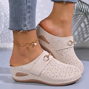 Close-up of beige wedge clogs featuring laser-cut floral patterns and metal ring strap
