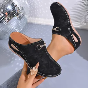 Detailed shot of black women's wedge mules featuring floral cutouts and a gold buckle