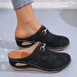 Detailed view of women's black suede platform clogs featuring a gold buckle and white stitching