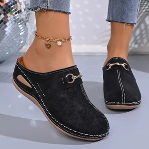 Detail view of black wedge mules featuring hollow-out floral pattern and metal buckle