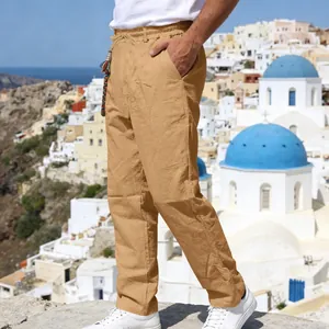 Men's loose khaki linen pants with drawstring waist shown against a scenic coastal town background