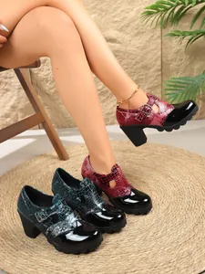 Primer plano de zapatos de charol con tacón grueso, textura de cocodrilo y hebilla.