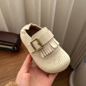 Close-up van retro crème lederen kinderschoen met franje en gouden gesp detail