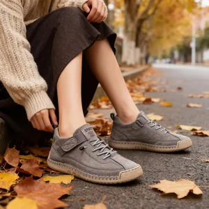 Nahaufnahme grauer lässiger genähter Stiefel auf einer herbstlichen Straße mit Laub