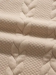 Macro view of beige jacquard fabric texture with diamond and leaf quilted patterns
