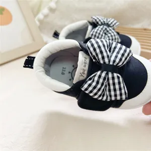 Close-up of baby walking shoe featuring a black and white checkered bow detail