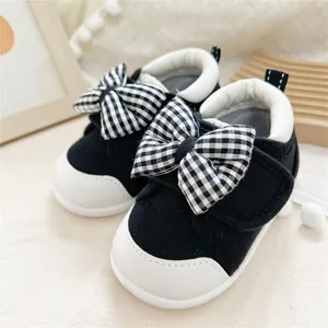 Close-up detail of black and white baby walking shoes featuring a large checkered bowknot