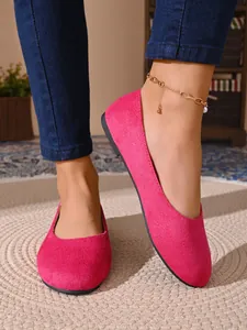 Dettaglio di eleganti ballerine in camoscio rosa acceso con punta tonda su un tappeto intrecciato