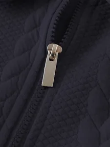 Close-up detail of the silver metal zipper pull and navy blue quilted jacquard fabric texture.