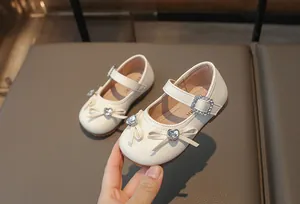 Nahaufnahme von weißen Prinzessinnenschuhen für Mädchen mit Strassherz-Schleife und Schnalle