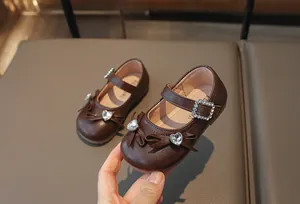 Detail von braunen Mädchen-Prinzessin-Schuhen mit Strass-Herz und Schleifenverzierung.