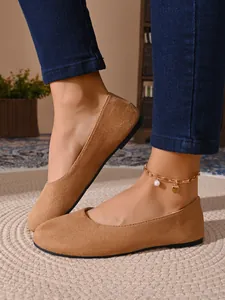 Dettaglio di ballerine scamosciate color cammello a punta tonda con jeans blu eleganti.