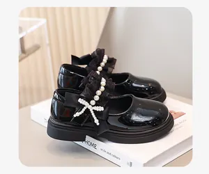 Dettaglio delle scarpe in pelle verniciata nera per bambine con fiocco di pizzo e perle