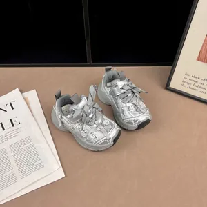 Detalle de zapatillas gruesas de malla plateada para niñas con lazos decorativos.