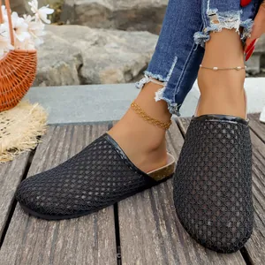 Detailed close-up of women's black woven mesh flat mules on a wooden deck outdoors.