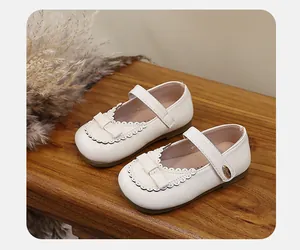 Detailed view of cream girls Mary Jane shoes with bow and scalloped edges on wood.