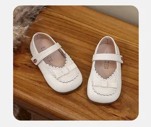 Close-up of white girls Mary Jane shoes featuring delicate bow and scalloped edges