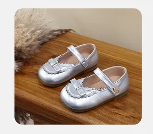 Close-up of silver girls' Mary Jane shoes with bow detail on a wooden surface
