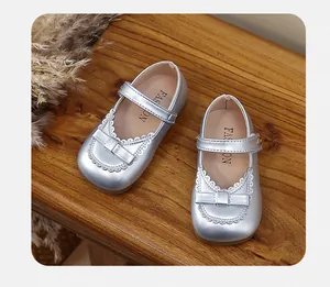 Close-up of silver girls' Mary Jane shoes with bow detail on a wooden surface.