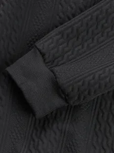Close-up detail of black men's knit sweater with intricate jacquard texture and ribbed cuff.
