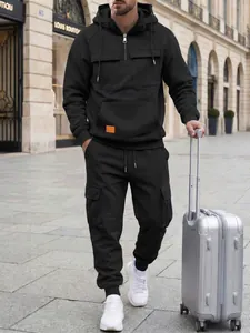 Full view of men's black cargo tracksuit set styled with a suitcase in street context