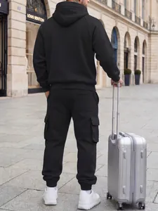 Back view of man wearing black hooded tracksuit and cargo sweatpants with a suitcase.