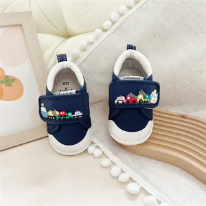 Close-up of baby walking shoes featuring cartoon car appliques on navy canvas straps