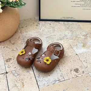 Detailed view of girls' brown T-strap shoes with crochet flowers and bows decoration.