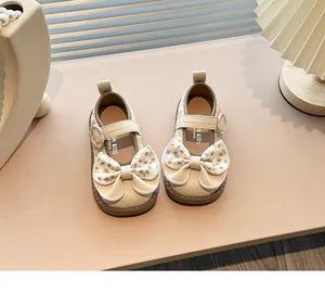 Close-up of girls' beige Mary Jane shoes with quilted toe and floral bow detail