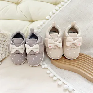 Detailed view of infant girl's heart print bow shoes in beige and grey colors