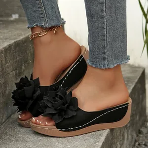 Détail de sandales compensées noires avec fleur 3D, portées sur des marches en béton.