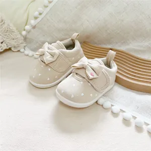 Close-up of beige baby girl walking shoes featuring a white heart pattern and bow.