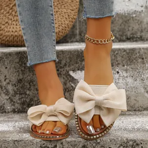 Primer plano de sandalias planas beige con un lazo de tela grande en escalones.