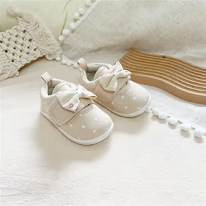 Detail of cream baby girl walking shoes with heart print, soft white soles and cute bows.