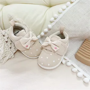 Close-up of beige baby girl walking shoes featuring a delicate bow and heart pattern detail