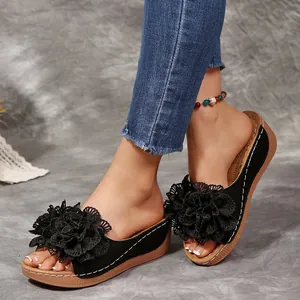 Gros plan de mules compensées noires avec fleurs en dentelle et coutures blanches