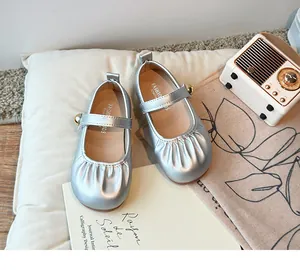 Close-up of silver metallic girls' princess shoes with pleated toe and gold ball strap.