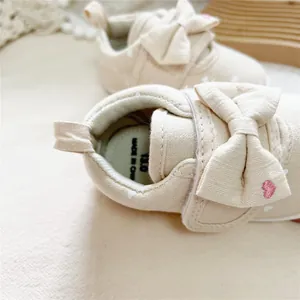 Detailed close-up of beige girl's walking shoes featuring a large bow and pink heart