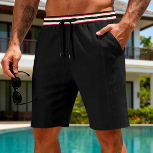 Detail shot of black quick-dry shorts on a model by the pool with striped waistband
