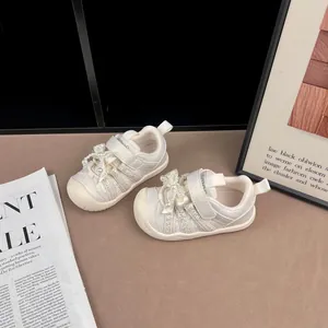 Nahaufnahme der schicken cremefarbenen Mädchenschuhe mit Perlenbogen und Klettverschluss