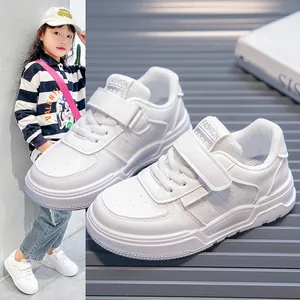 Side view of white kids' sneakers with hook-and-loop straps on a textured grey background