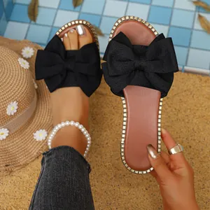 Primer plano de sandalias negras con lazo y elegante tobillera de perlas de mar