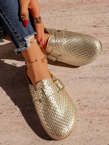 Gros plan de haute qualité montrant la texture tressée dorée de ces mules élégantes.