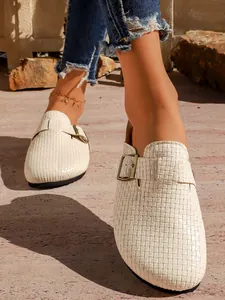 Détail de sabots compensés tressés blancs avec boucle en bronze réglable portés par mannequin