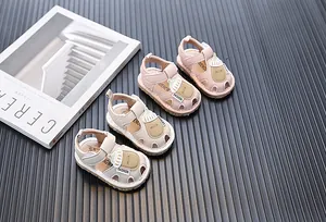 Nahaufnahme niedlicher Baby-Lauflern-Sandalen mit Cartoon-Milchflasche in Pink und Beige