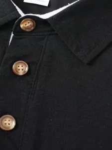 Primer plano detallado de los botones jaspeados marrones en el cuello de un polo negro de hombre