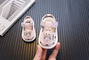 Primer plano de sandalias rosas para bebé con conejo de dibujos y cierre de velcro.